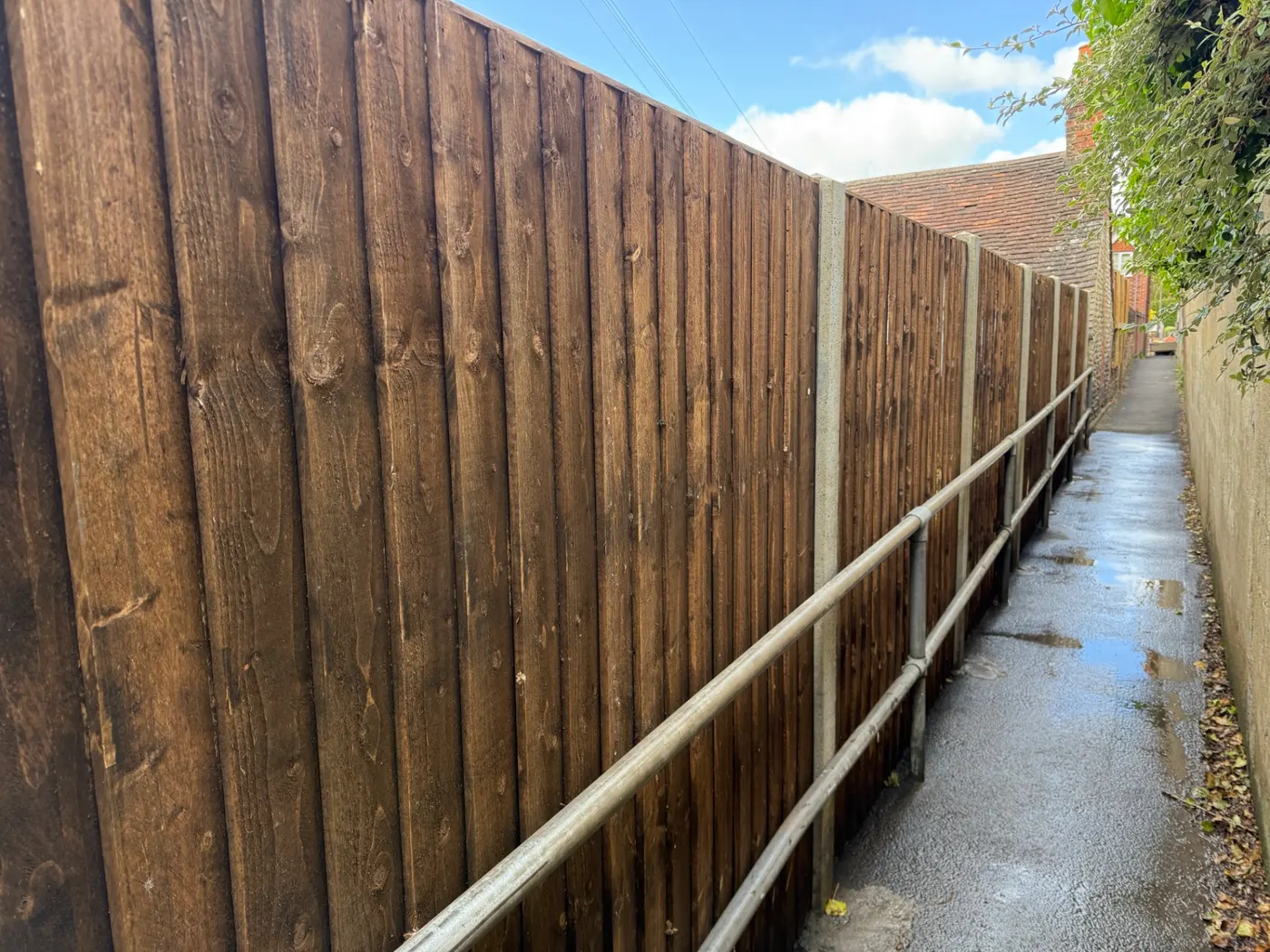 Dark stained closeboard fence with concrete posts along an alleyway